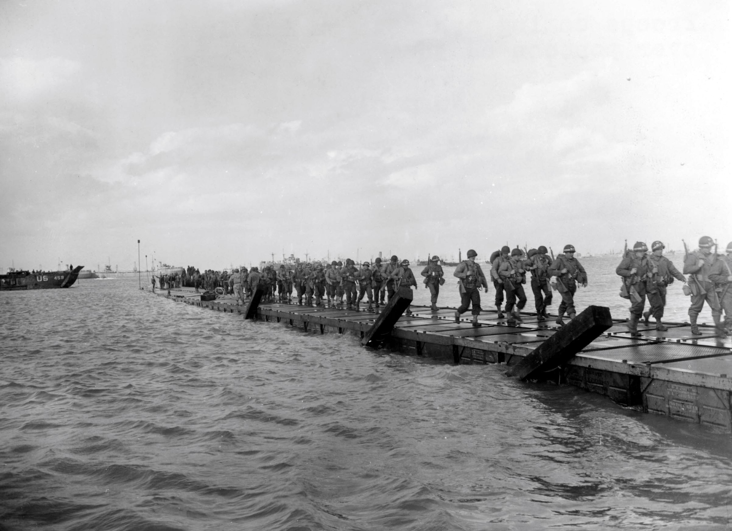 Soldiers marching ashore across pontoon causeways, most likely at Utah Beach.